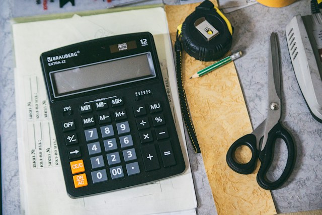 Planning tools on a desk including a calculator, pencil, tape measure, and scissors